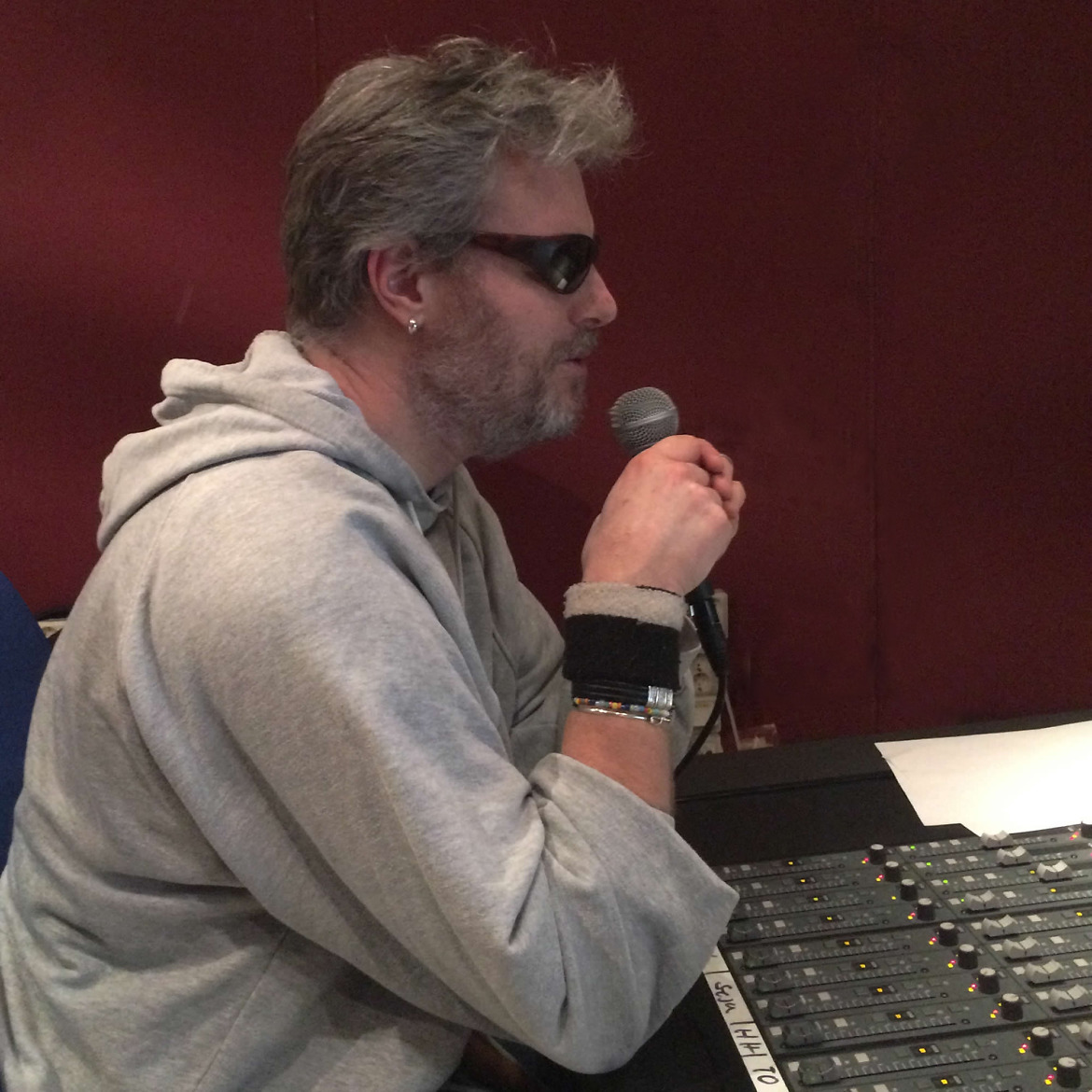 Johan Seige vid musikstudions mixerbord i kontrollrummet, pratandes i mikrofon till musiker i inspelningsrummet.